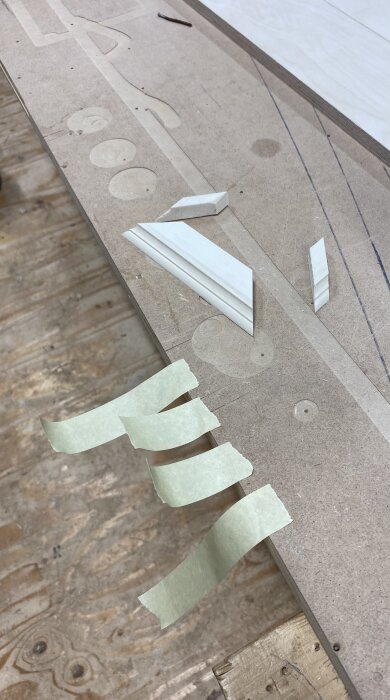 Små träbitar i olika former och storlekar ligger utlagda på en arbetsbänk, med bitar av tejp arrangerade bredvid dem.