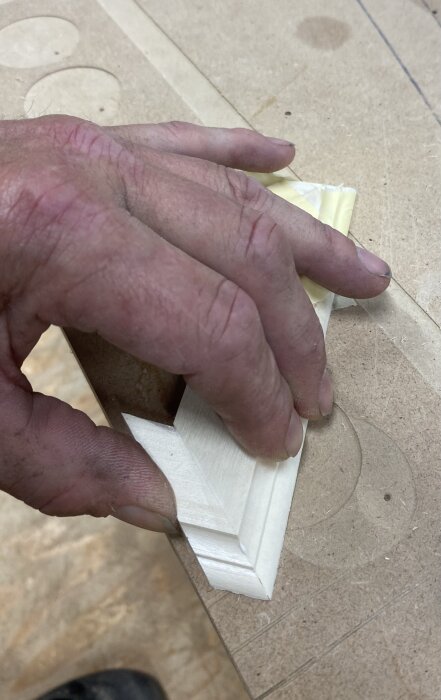 En hand håller i en liten listbit med yttergering på en arbetsbänk, för renovering och dekoration av dörröppning.