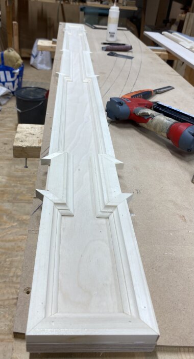 Trälist med dekorer på arbetsbänk, omgiven av verktyg och material i verkstadsmiljö.