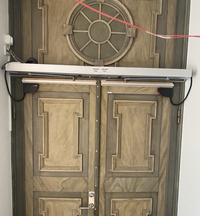 Dörr med träramar och monterad dörautomatik, kablar synliga.