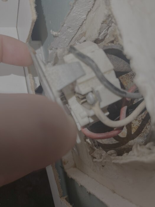 Närbild av ett perilex-uttag med exponerade kablar (svart, vit, röd) och ett fingergrepp vid sidan av väggen.