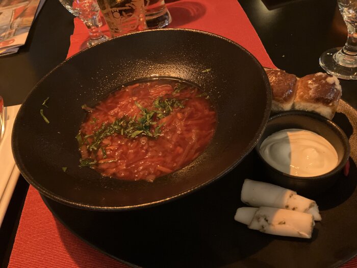 Skål med borsjtj toppad med örter, serverad med bröd, rullad ost och en skål gräddfil.