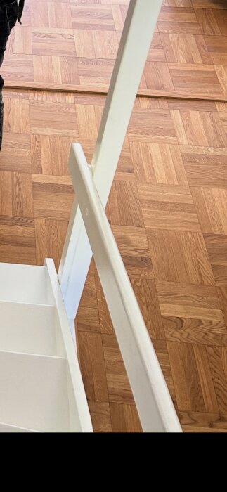 Trägolv i rutparkettmönster i ek med vitmålad trappa delvis synlig i förgrunden.