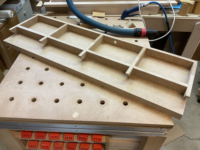 Torsionbox av MDF i snickarverkstad, perfekt för att stärka ett högt anhåll på justersåg, med hål och sektioner för montering och stabilitet.