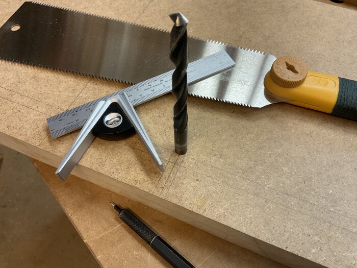 Mätverktyg, borr, och japansåg på en MDF-skiva med ritsade linjer för ett gör-det-själv projekt.
