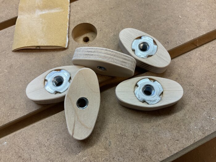 Handgjorda vred av björkplywood med islagsmuttrar på en arbetsbänk, sandpapper i bakgrunden.