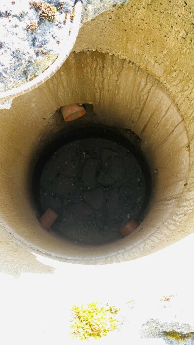 Brunn med tre rör, belägen i en grävd kulle, inifrån sedd med fuktig mark i botten och röröppningar synliga på insidan.