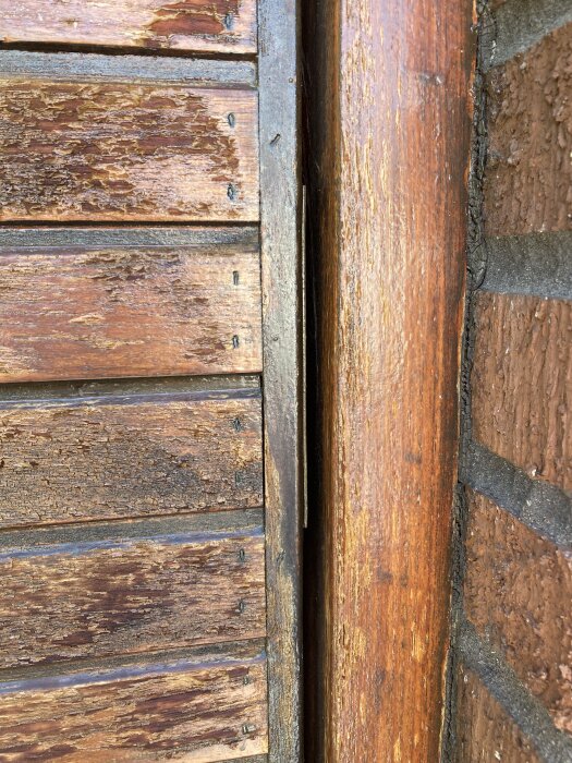 Sliten träpanel på garageport med synliga sprickor och avflagningar, intill en tegelvägg.