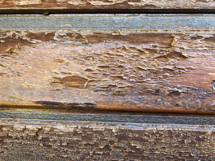 Närbild av en träyta med flagnande färg som behöver slipas och oljas, enligt inlägg om underhåll av garageportar.