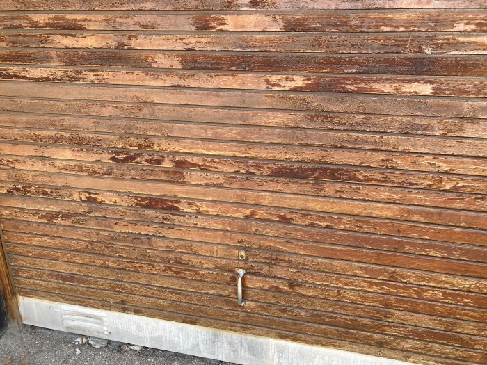 En trägarageport med sliten och flagnande yta, som behöver slipas och oljas enligt diskussionsråd.