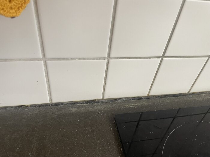 Ojämn kant på köksbänkskiva framför vitkaklat kök; bristfälligt borttagen silikonfog syns tydligt vid skarven mellan bänk och kakel.