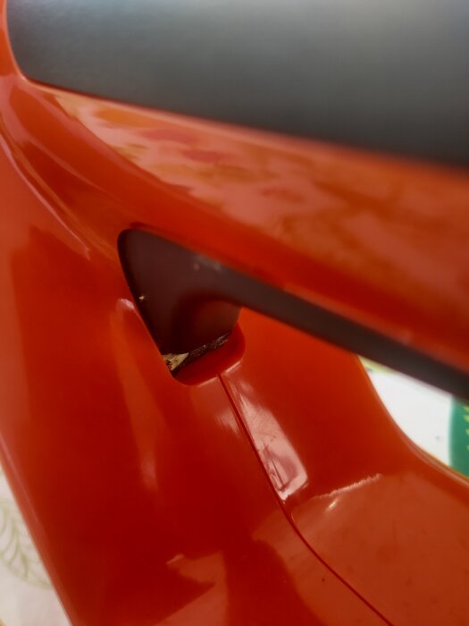 En närbild av en orange plastdel med en spricka eller skada nära en skruvanslutning.