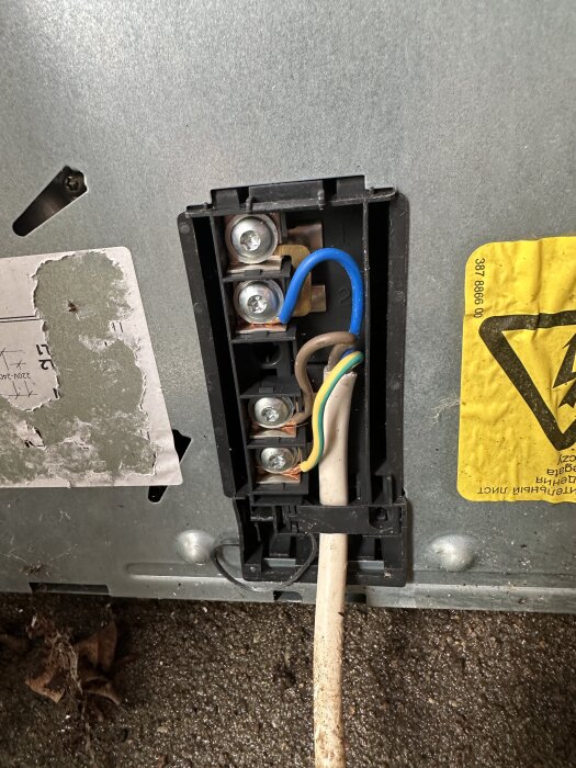 Elanslutning med kabelkoppling för byte av stickpropp på en spis, med synliga ledningar i blått, brunt och grönt/gult i hölje.