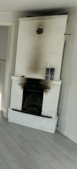 Vit kamin med sotfläckar, två flaskor rengöringsmedel ovanpå.