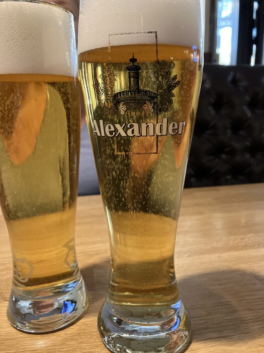 Två ölglas på ett träbord, det ena glaset har texten "Alexander" på sig.