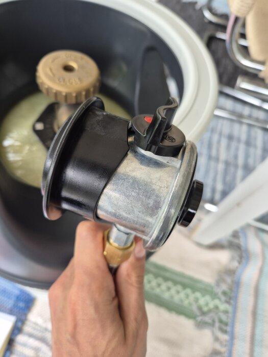 Gasregulator för ogräsbrännare hålls i en hand, bredvid en gasbehållares ventil.