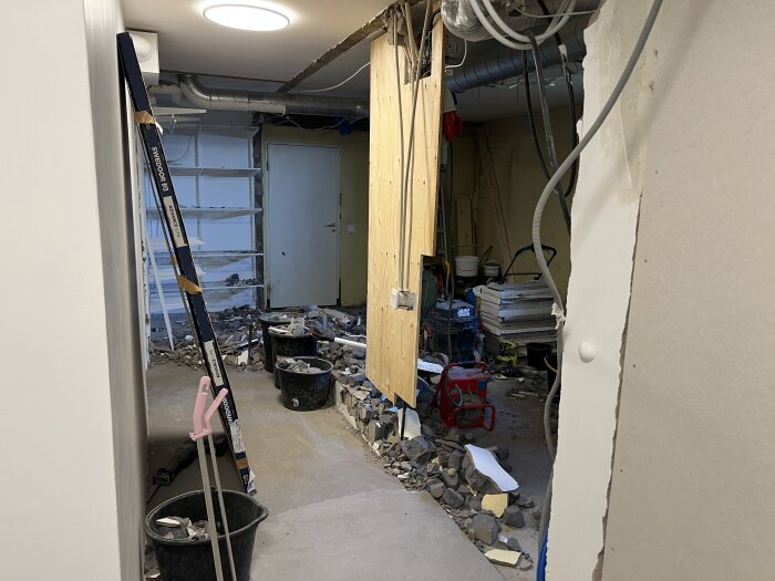 Renoveringsprojekt med en riven innervägg, exponerat isoleringsmaterial och verktyg som hinkar och stege i en byggarbetsplats.