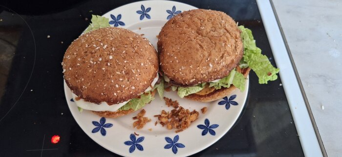 Två burgare med sallad, dressing, ost och rostad lök på en vit tallrik med blå mönster.