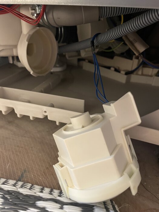 Närbild av diskmaskinens undermonterade sektion med avlägsnad del, synliga kablar och filter.