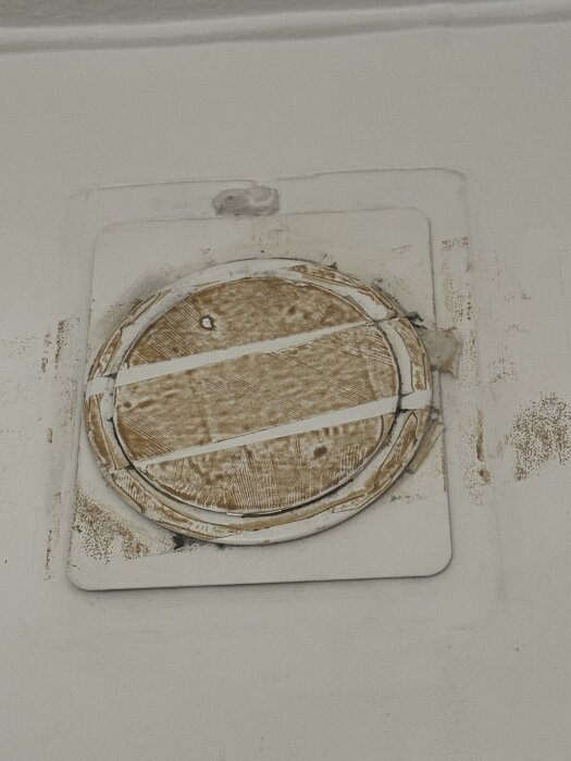 Ventil i sovrum med bruna tejprester och slitage på väggen runt ventilen.