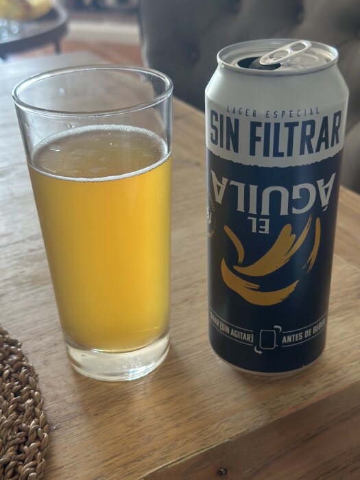 Ett glas med ofiltrerad lageröl bredvid en öppnad burk öl med texten "Sin Filtrar" på ett träbord.