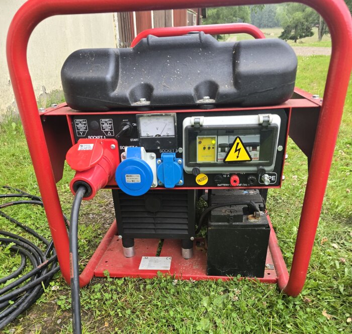 Bärbar elgenerator på gräsmatta med flera eluttag, voltmätare och en varningssymbol för elektricitet. Röd skyddsställning och ansluten kabel syns.