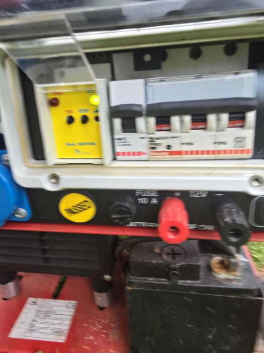 Reservkraftsaggregat med instrumentpanel, säkringar och anslutningar. Skydd och testknappar synliga samt anslutningar för batteri och strömkabel.