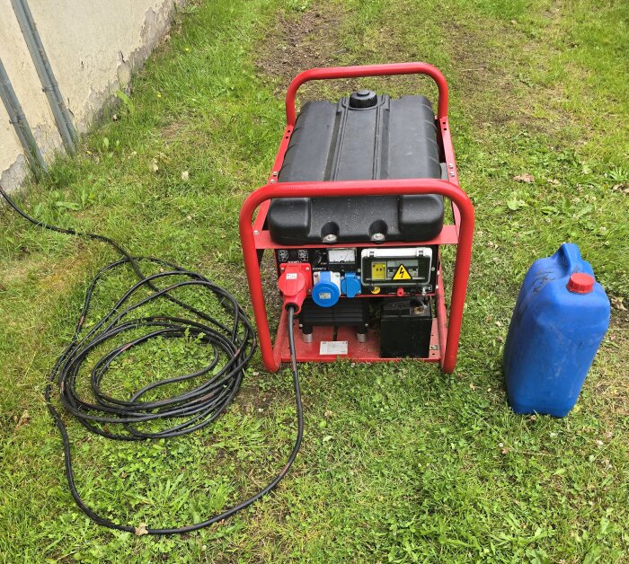 Bärbart elverk på gräs med röda handtag, anslutna kablar och en blå bränsledunk bredvid.