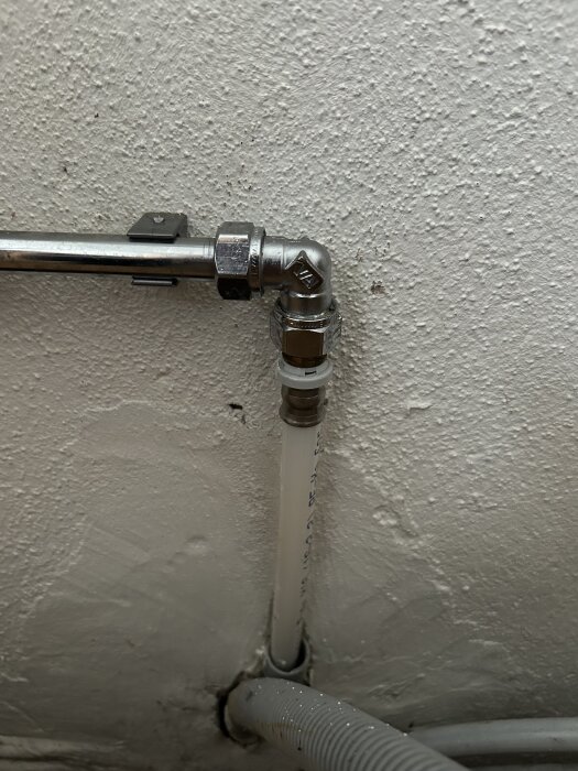 Metallrör kopplat med vinkelkoppling till en sladd på en vit vägg.