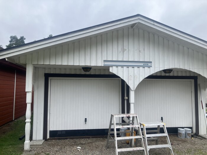 Vit garagefasad där dekorativa detaljer tagits bort, med två stegar och några målarburkar framför.