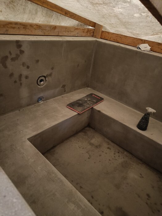 Betonghörn med nyspacklad yta, träreglar syns ovanför. Verktyg och sprayflaska placerade på betongytan.