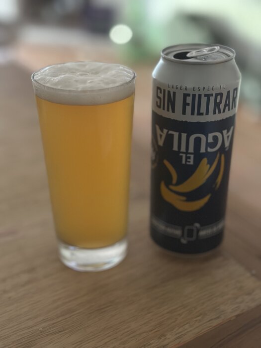 Ett glas skummande öl bredvid en burk öl märkt "Sin Filtrar" på ett träbord.