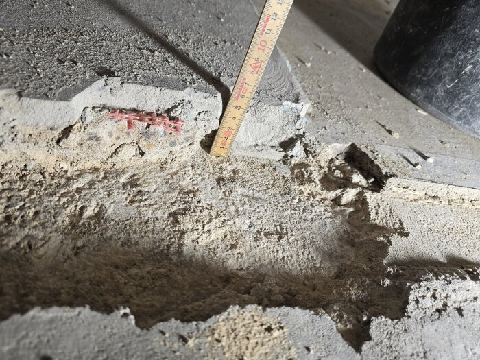 Ränna i betonggolv med måttstock och del av rött armeringsnät av glasfiber. Golvet har delvis avlägsnats för inspektion av underlag.