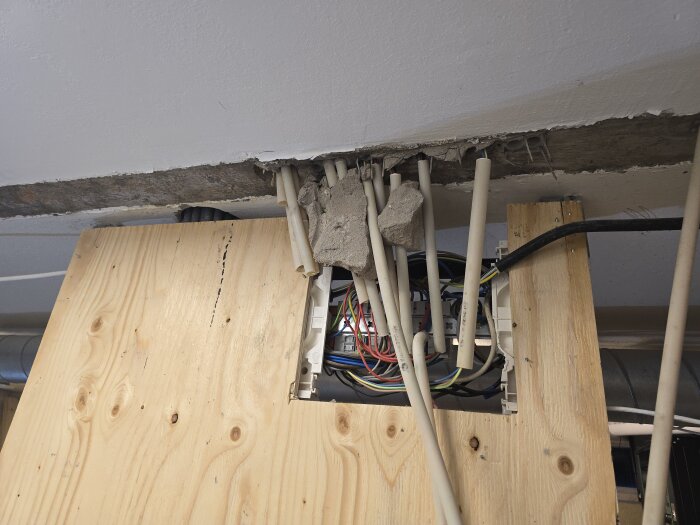 Elektriska kablar och VP-rör synliga i ett delvis öppnat väggparti av trä och betong, i samband med en husrenovering.