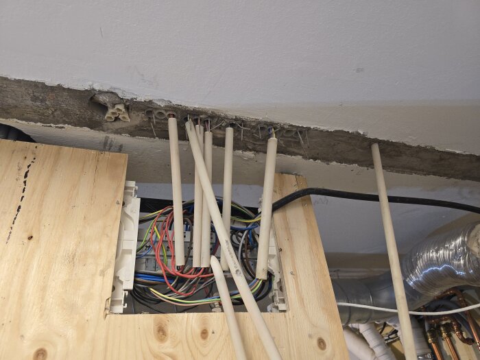 Elinstallation med VP-rör och kablar syns i en väggöppning gjord av träskiva. Rör och kablar är dragna genom en betongvägg.