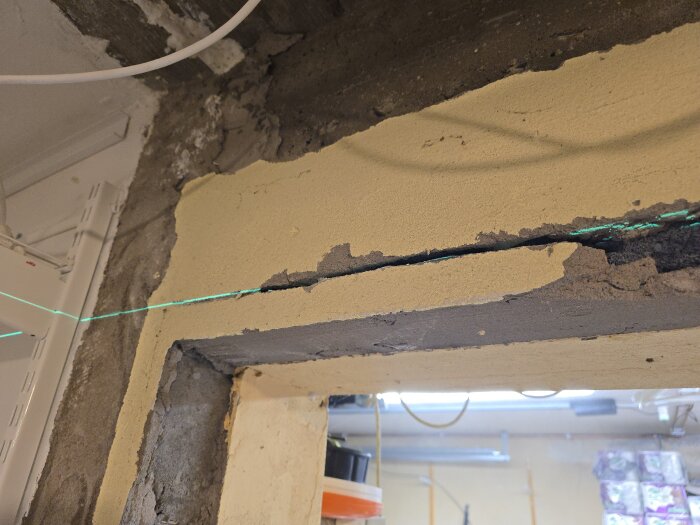 Överdel av en dörröppning med synlig blåbetong och laserlinje som används för att guida arbete i en källarrenovering.