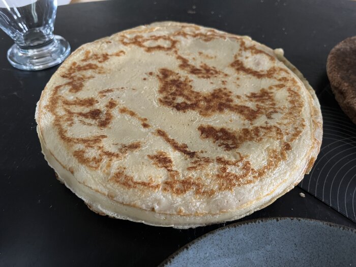 Pannkaka på ett bord med ett glas i bakgrunden, tillagad med utgången mjölk.