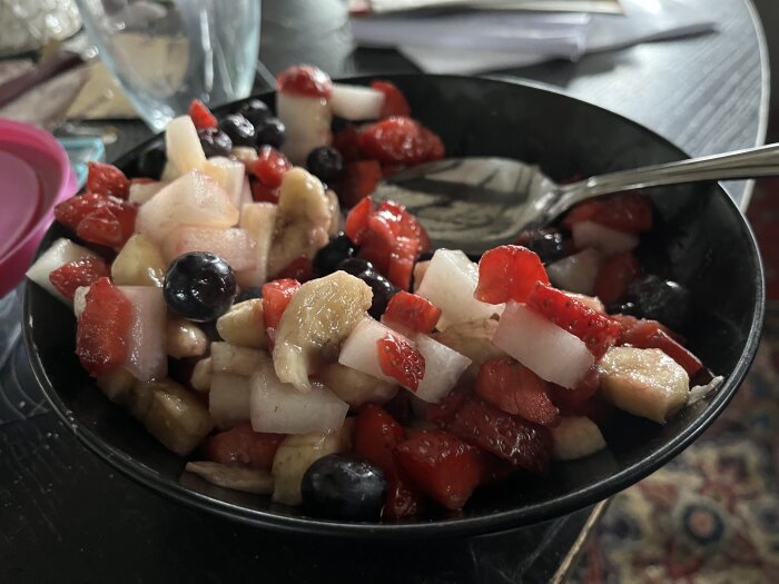 Skål med fruktsallad innehållande jordgubbar, bananer, blåbär och melonbitar.