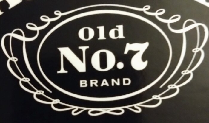 Etikett med texten "Old No. 7 Brand" inuti en dekorativ ram.