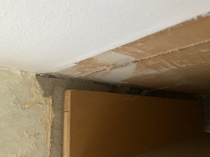 Venstre vegg av garderobe mot taket, med gipsskiver og synlig isolasjon. Veggen viser slitasje og dammer av fugemasse.