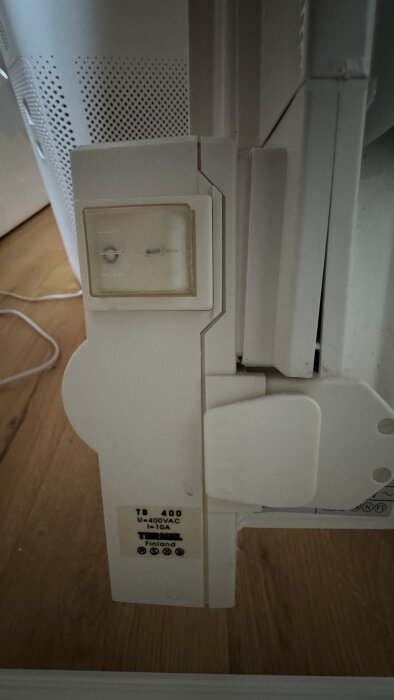 Gammalt väggmonterat 400V-element utan termostat, vit färg, trägolv i bakgrunden.