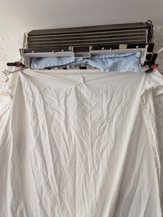 Rengjord luftvärmepump med tygskydd över vägg och tapet, visar "efter"-steg av rengöringsprocessen med Julas värmepumpsrengöring.