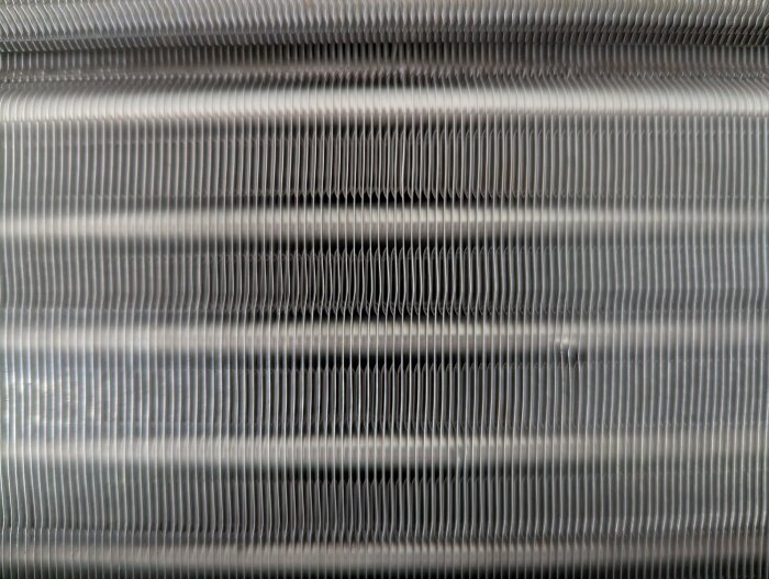 Rengjord trumma på luftvärmepump som visar vågformade metallfins efter rengöring med Julas värmepumpsrengöring och pensel, nästan helt rent.