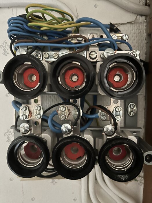 Bild av ett öppnat elcentral med sex säkringshållare, med oanslutna elkablar i överdelen, set uppifrån.