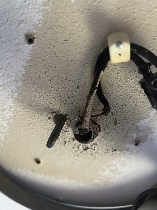 Gammal elektrisk installation med torr och sprucken ledning i tak, ovanför en metallplatta, med angränsande hål i ytan.