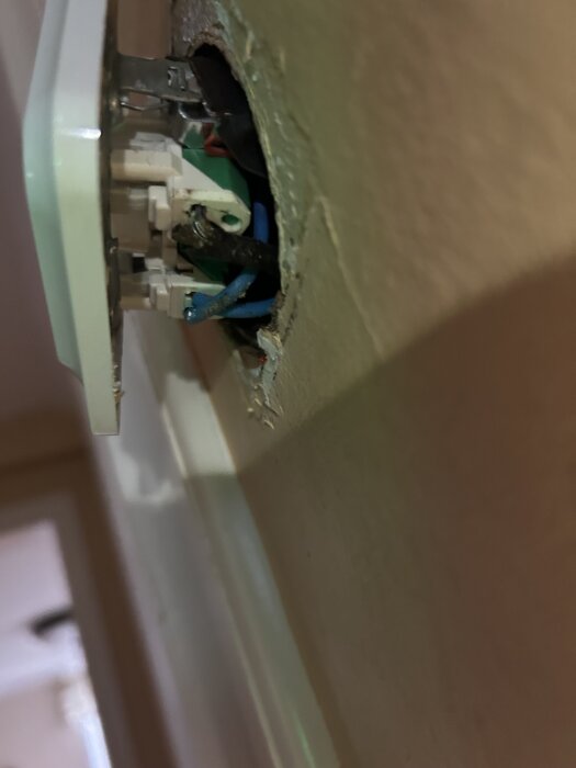 Närbild av en öppen vägguttag där gamla tygisolerade ledningar är synliga i en metallram.