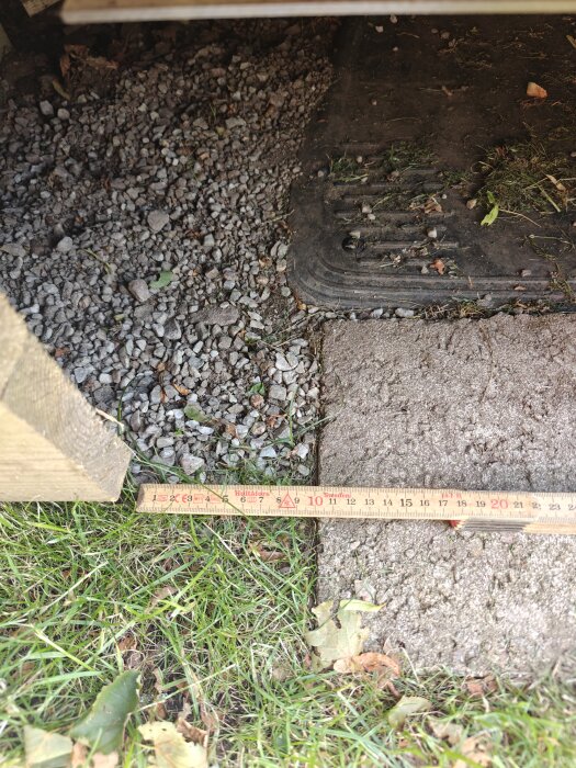 Måttband som mäter en 10 cm mellanrum vid kanten av gräs, grus och en stenplatta.