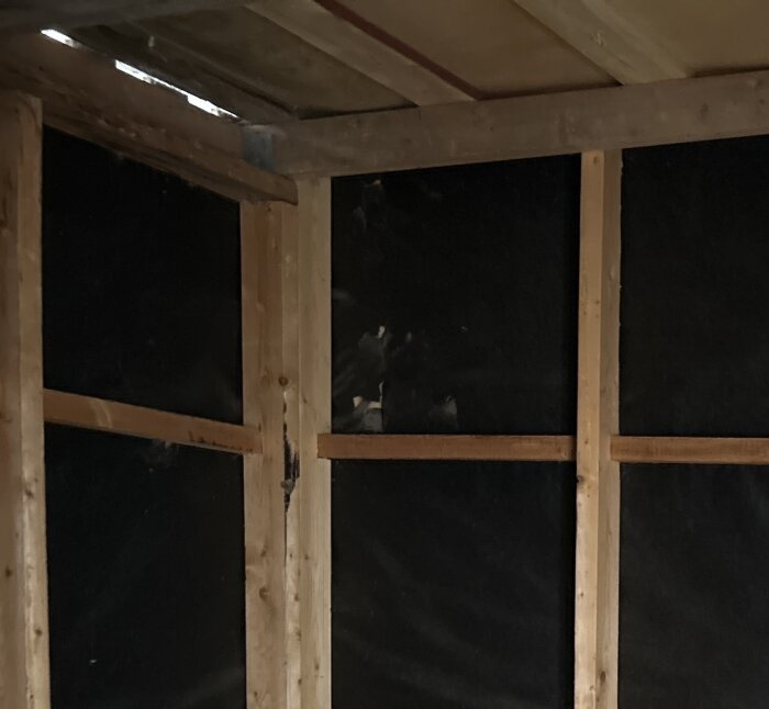 Hål i vindpappen inuti ett uteförråd med synliga träbalkar och mörka väggar, diskuteras om det behöver repareras eller bytas ut.