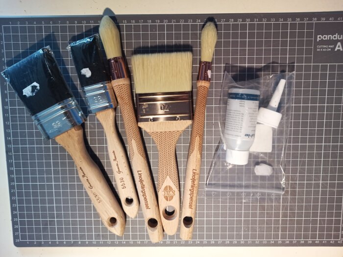 Fyra penslar av märkena Gnesta och Scandinavian Window Craft samt flaska med olja på en skärmatta.