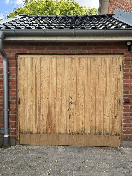 Nyslipad garageport i trä efter borttagning av gammal linoljefärg, omgiven av tegelväggar och med ett svart tak ovanpå.